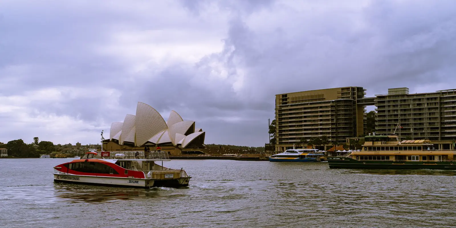 Scenic view of Sydney Opera House and bustling harbor in cloudy weather, New South Wales, Australia.