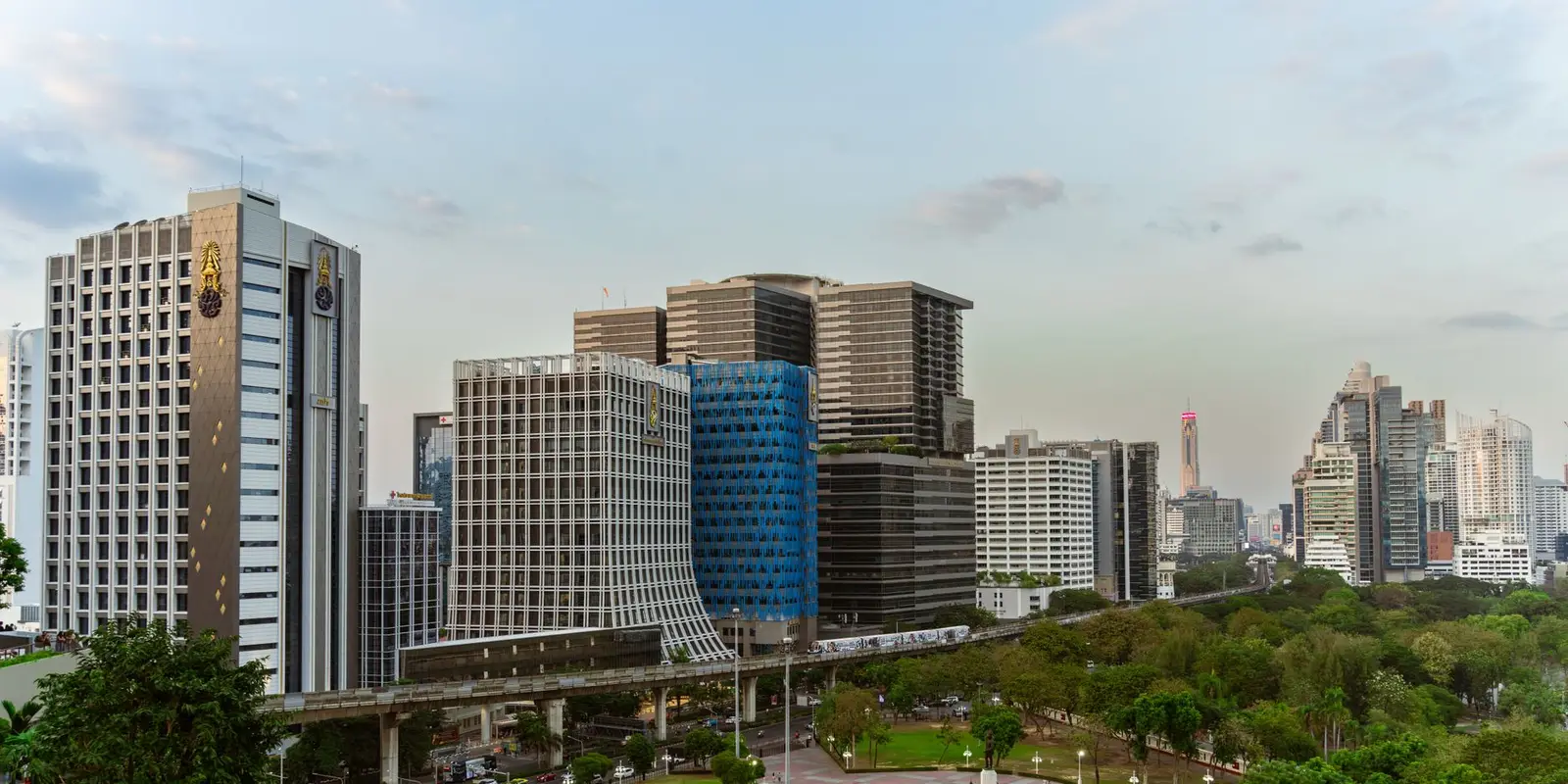 Aerial view of modern skyscrapers and greenery in Bangkok city during daytime, showcasing urban architecture.