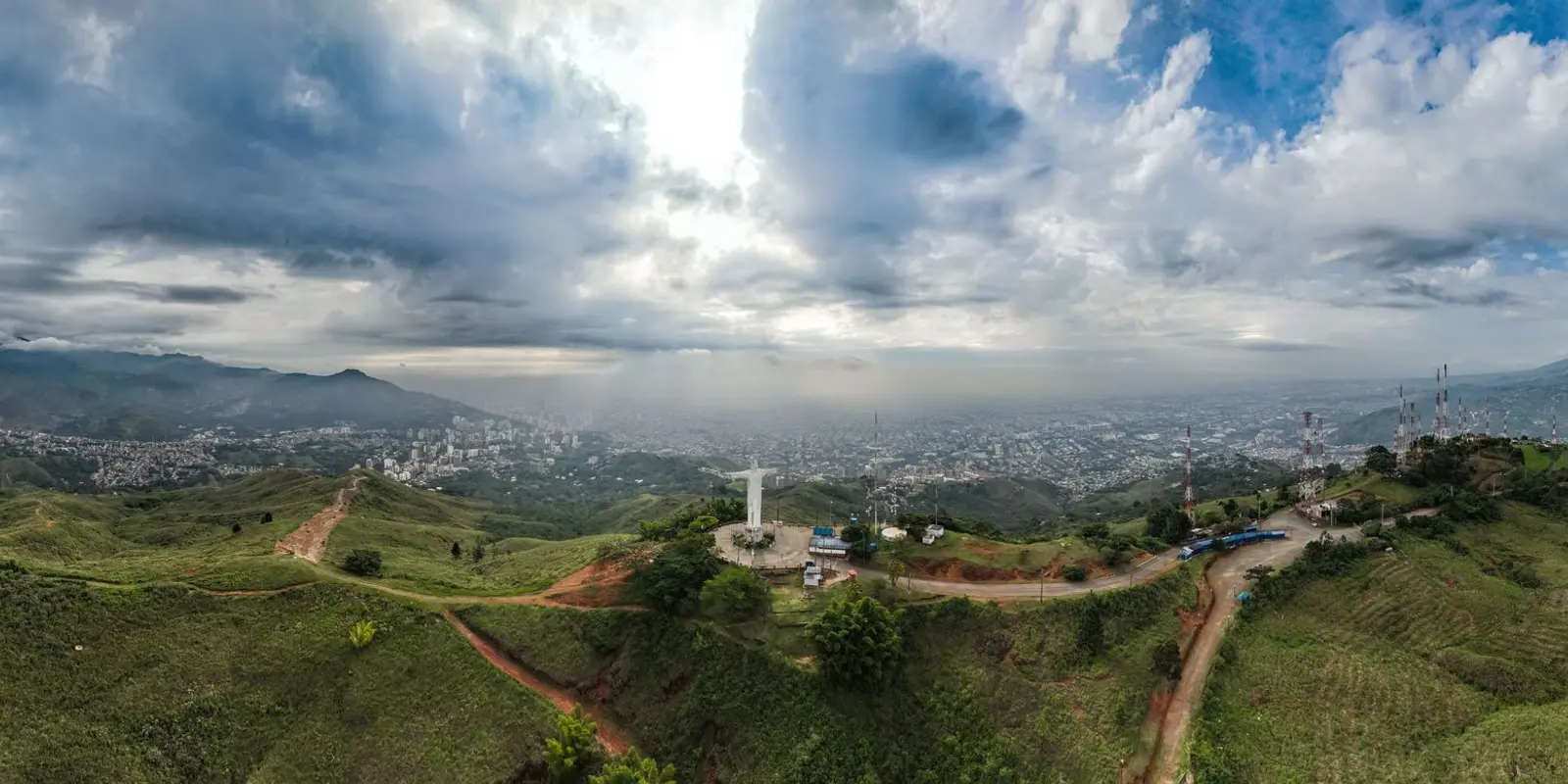 Stunning aerial panorama of Cali, Colombia featuring Cristo Rey statue under dramatic skies.