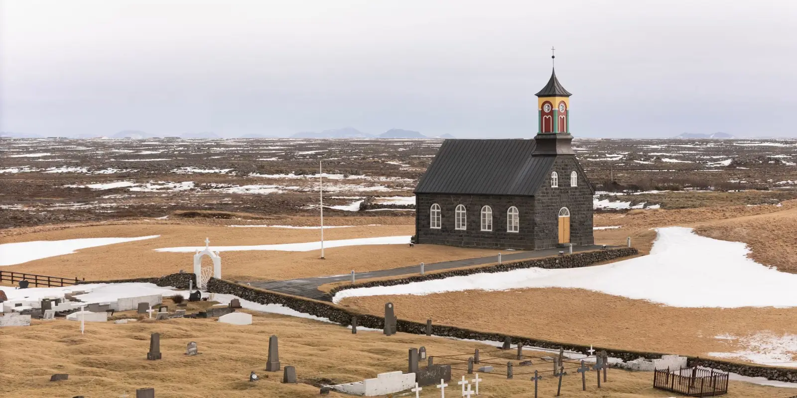 A scenic view of a historical church and graveyard surrounded by Icelandic nature during early spring in Suðurnesjabær, Iceland.