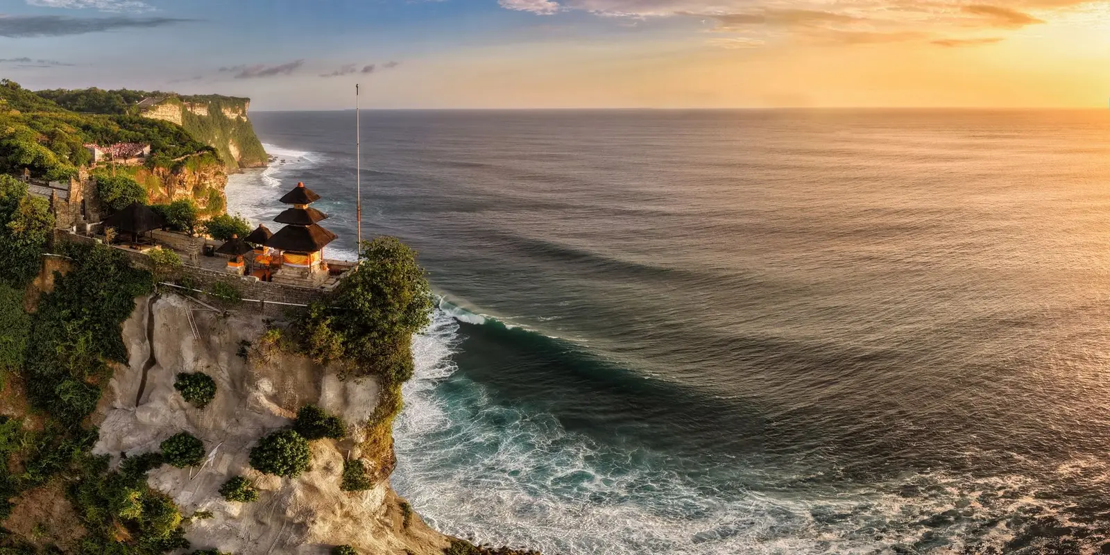A breathtaking aerial view of Uluwatu Temple perched on cliffs overlooking the ocean at sunset in Bali, Indonesia.