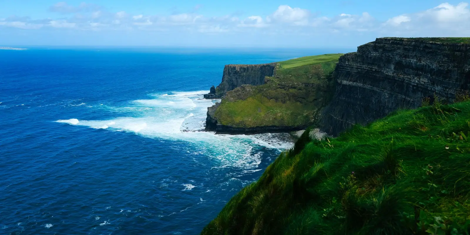 Breathtaking view of the Cliffs of Moher with expansive ocean and lush greenery under a bright sky.