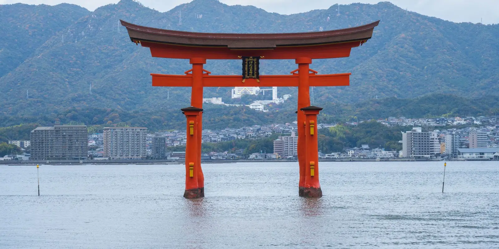 Scenic view of the floating Torii gate at Itsukushima Shrine in Japan, with mountains and sea.