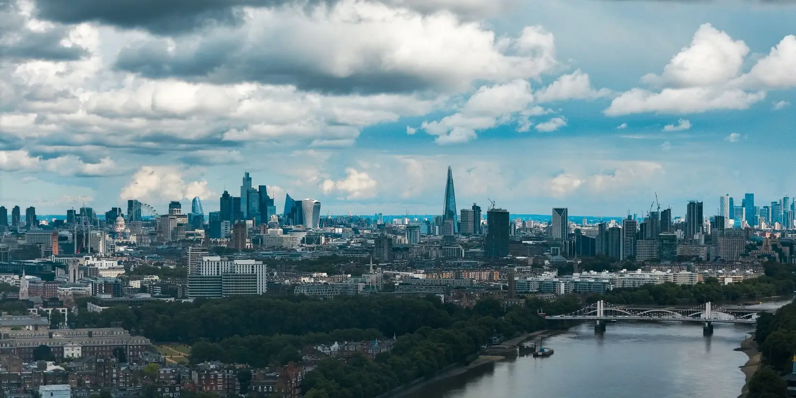 Wide-angle view of London's modern skyline and River Thames under a dramatic sky.