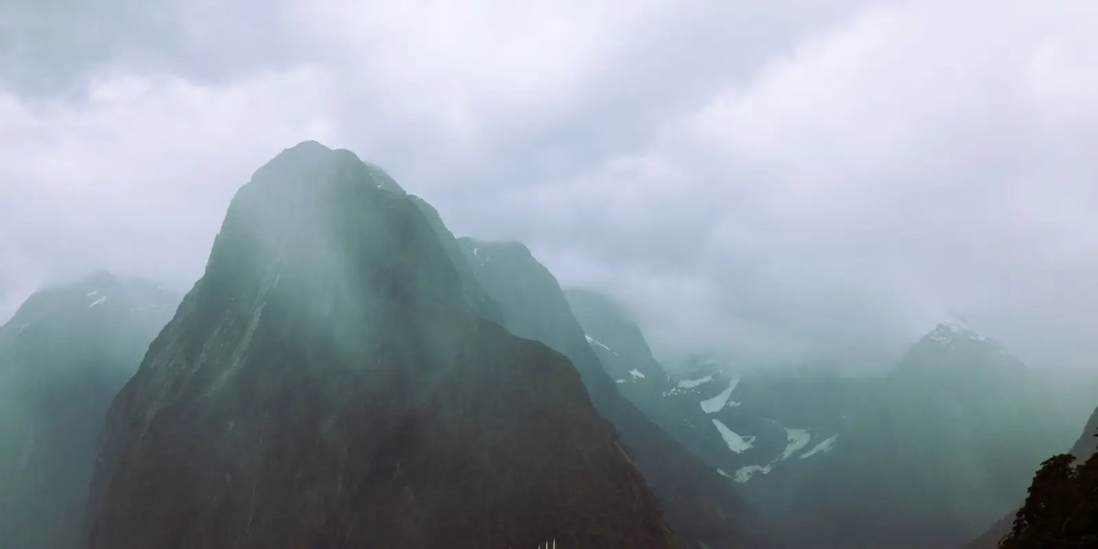 A sailboat navigating the dramatic and cloudy landscape of Milford Sound.