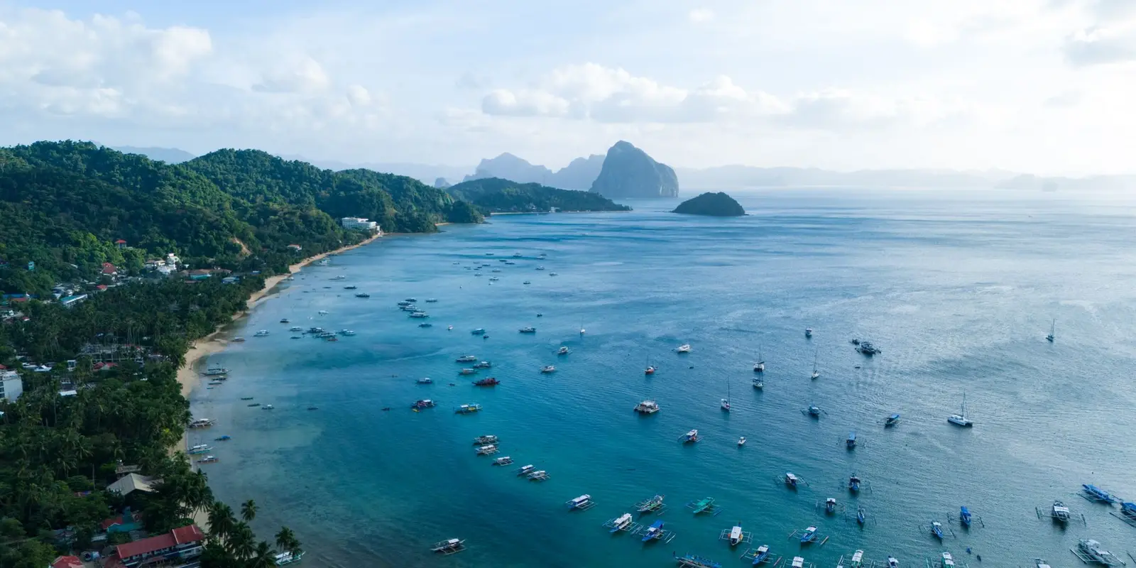 Stunning aerial view of El Nido's vibrant blue bay with lush greenery and boats, capturing the essence of the Philippines' natural beauty.
