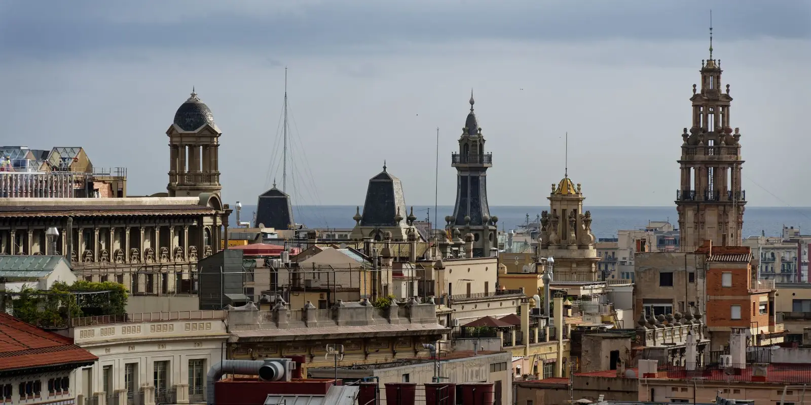 Panoramic view of historic architecture and bell towers in Barcelona, Spain with the sea in the background.